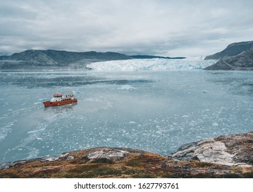 Red Passenger Cruise Ship Sailing Through The Icy Waters Of Qasigiannguit, Greenland With Eqip Sermia Eqi Glacier In Background. Ice Breaking Off From Calving Glacier. A Small Boat Among Icebergs