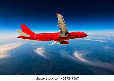 Red Passenger Plane In Flight. Aircraft Flying High Above The Ground And Cirrus Clouds.