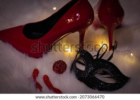Red patent high-heeled shoes, black carnival mask and lights on a white fluffy rug