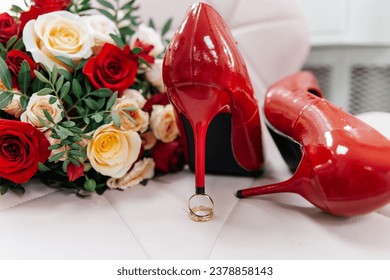 Red patent leather shoes of the bride near gold wedding rings and a bouquet of roses