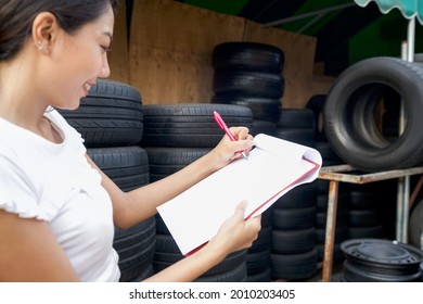 Red Pen, Paper And Clipboard In Owner Of The Auto Parts Store Hand. Several Car Tires Are Lined Up In A Tire Shop.