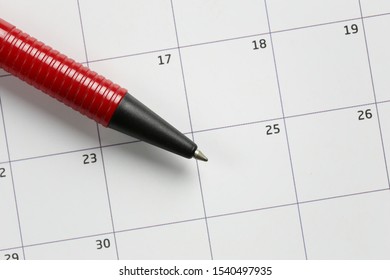 Red pen pointing to twenty-fifth number of December on paper calendar is Christmas Day concept.
