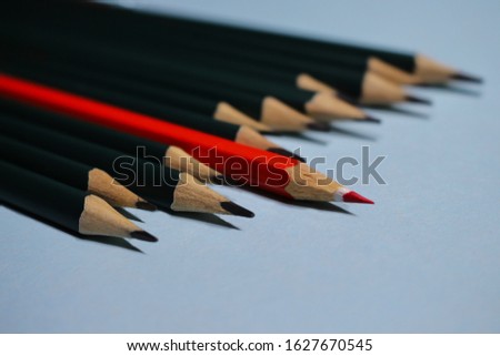 Red pencil standing out from crowd of plenty identical black fellows on blue background.  Leadership, uniqueness, independence, initiative, strategy, dissent, think different, business success concept