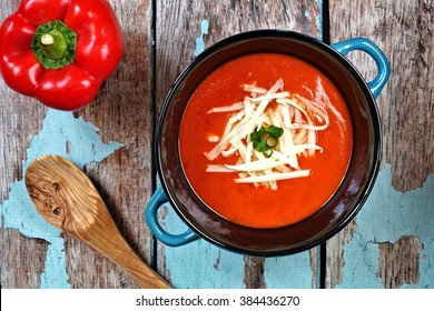 Red Pepper Soup Topped With Shredded Cheese And Green Onions, Overhead Scene On Rustic Blue Wood Background