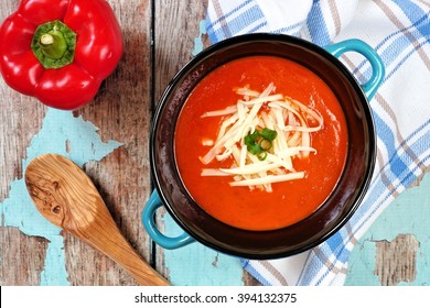 Red Pepper Soup Topped With Shredded Cheese And Green Onions, Overhead Scene On Rustic Blue Wood Background