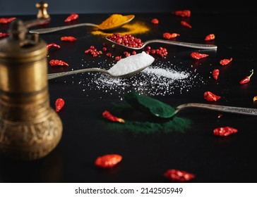 red pepper  tumeric , chili peper,  white salt and spirulina in vintage spoons on black background. Arrangement of different types of spices in tea spoons and an spices grinder