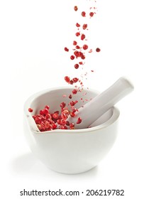 Red Peppercorns Falling Into Mortar And Pestle On A White Background