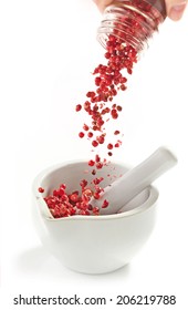 Red Peppercorns Falling Into Mortar And Pestle On A White Background