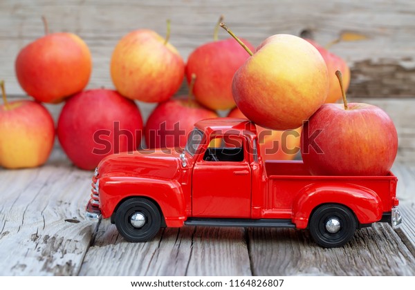Red\
pick up car with apple harvest. Autumn and harvest concept. On\
wooden background. Natural light, selective focus.\
