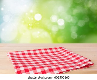 Red picnic cloth folded on wooded table with green nature blurred background.Empty napkin advertisement concept.