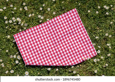 Red picnic tablecloth. Red checkered picnic blanket on a meadow with daisies in bloom. Beautiful backdrop for your product placement or montage. Topview.