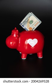 Red Piggy Bank In The Form Of A Cow With 100 Dollars On A Black Background. Investing And Storing Money. The Concept Of Frugality And Financial Literacy.