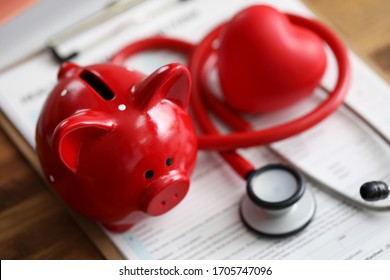 Red piggy bank stethoscope and toy heart lying at health insurance claim application form closeup