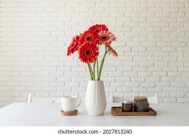 Red and pink gerbera daisies in white vase on kitchen table with candles and cup, minimal style - Powered by Shutterstock