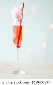 Red Pink Sparkly Bubbly Drink In A Champagne Glass With Pink Cotton Candy On Top Of The Glass. Small Light In The Background, Light Background, Minimalistic