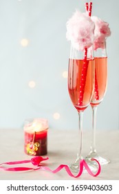 Red Pink Sparkly Bubbly Drink In A Champagne Glass With Pink Cotton Candy On Top Of The Glass. Small Light In The Background, Light Background, Minimalistic