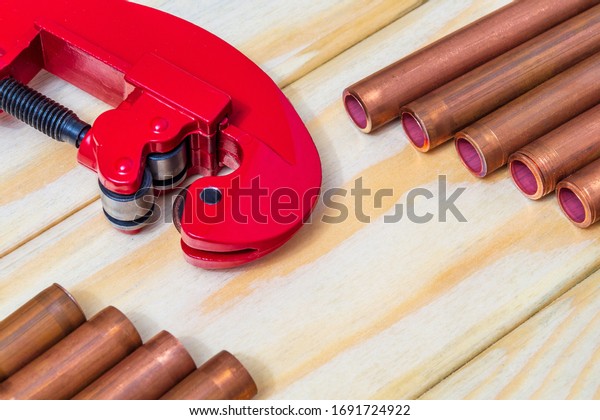 Red pipe cutter and\
copper pipes with connectors for plumbing repairs on vintage wooden\
boards close up