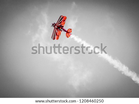 Red plane with propeller flying upward with white smoke