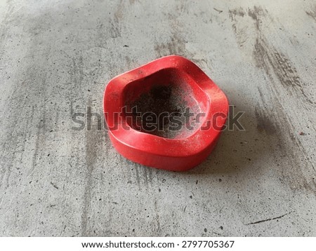 Red plastic ashtray with cigarette ash on industrial concrete floor background