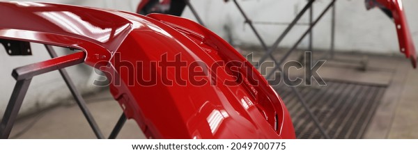 Red plastic car bumper drying after repainting in\
spraying booth