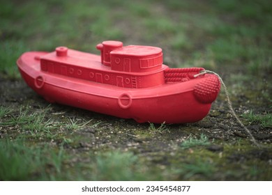 A red plastic children's boat is standing on dry land. Shallowing of the riverbed.The end of shipping.Drought.
