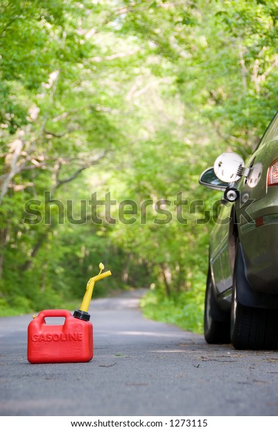 A red plastic gas can sitting in the\
middle of a country road next to a stranded\
car.