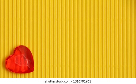 Red Plastic Heart On Yellow Corrugated Background With Vertical Pattern, Sign Of Love And Romance, Greeting Card For Womens Day Or Valentine