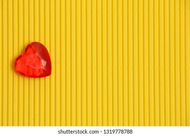 Red Plastic Heart On Yellow Corrugated Background With Vertical Pattern On Left Side, Sign Of Love And Romance, Greeting Card For Womens Day Or Valentine