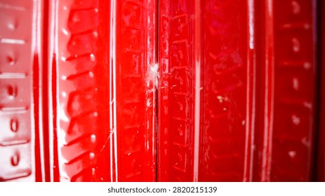 Red plastic surface with embossed vertical patterns. Center shows small crack, slightly glowing. Texture reflects light, emphasizing depth and detail. Close-up shot highlights durability and wear