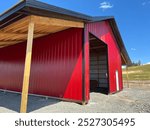 “Stunning red pole barn under construction, featuring 29-gauge red metal walls and a sleek black roof. A modern, durable structure in progress, blending bold colors with strong craftsmanship.”