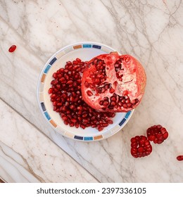 Red pomegrant seeds in plate with marble background.
