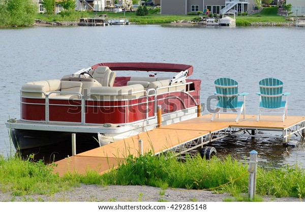 Red Pontoon\
Boat Tied to a Dock With Two\
Chairs