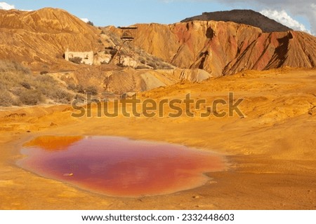 Red pool of contaminated water forms in front of pit head at abandoned mine in mazzaron murcia spain showing rusty pit head winch and arid rocks stained from mineral deposits