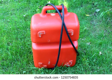 Red Portable Plastic Fuel Tank 24-25 Liters With Handle And Tube For Outboard Motor In Summer On Green Grass - Motor Boat Trip