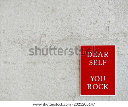 Red poster on copy space white wall with text message DEAR SELF YOU ROCK, positive self talk to raise self esteem, daily beautiful affirmation to remind strength and ability to overcome difficulties