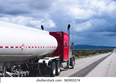 Red powerful classic big rig semi truck with high exhaust pipes pulling a trailer with a tank intended for the carriage of liquid hazardous flammable cargo transports petrol on the road in Nevada