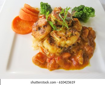 Red prawn curry on basmati rice with vegetables on the side served on a white porcelain plate - Shutterstock ID 610423619