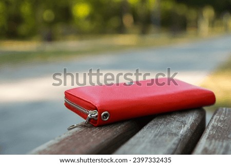 Red purse on wooden bench outdoors, space for text. Lost and found