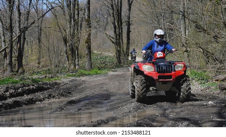 A Red Quad Bike With A Girl Behind The Wheel Is About To Drive Through A Puddle In The Spring Woods. Front View. Extreme Type Of Outdoor Activities. ATV Riding