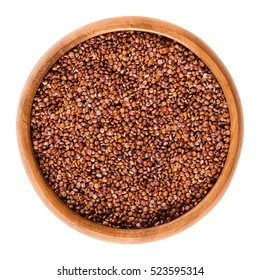 Red quinoa seeds in wooden bowl. Edible fruits of the grain crop Chenopodium quinoa in the Amaranth family is a pseudocereal and used cooked. Isolated macro food photo close up from above on white.