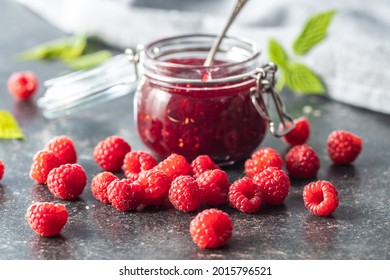 Red Rasberries Jam In Jar And Ripe Raspberries On Black Table.