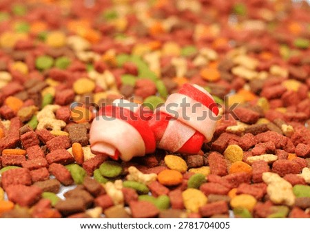 Red rawhide dog chew bone placed on colorful dry pet food background.