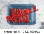 Red recall warning message over tray of raw ground beef, flat lay