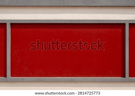Red rectangular wall panel framed by grey concrete borders on a building exterior.