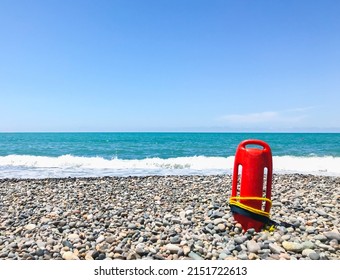 Red rescue float on rocky beach with sea panorama and no lifeguard. Static blank space copypaste background safety concept