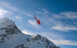 Red Rescue Helicopter Flying Over The View Of The Snowy Rocks In Alpine Ski Resort Zermatt Near Matterhorn Mountain. Winter Nature Landscape Of Swiss Alps. Mountains With Snow In Switzerland.