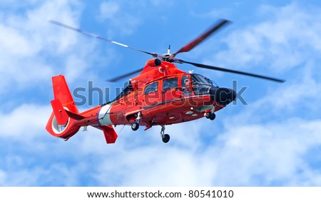 Red rescue helicopter moving in blue sky with blur propeller