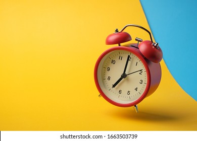 Red retro alarm clock floating in the air with yellow and blue background.