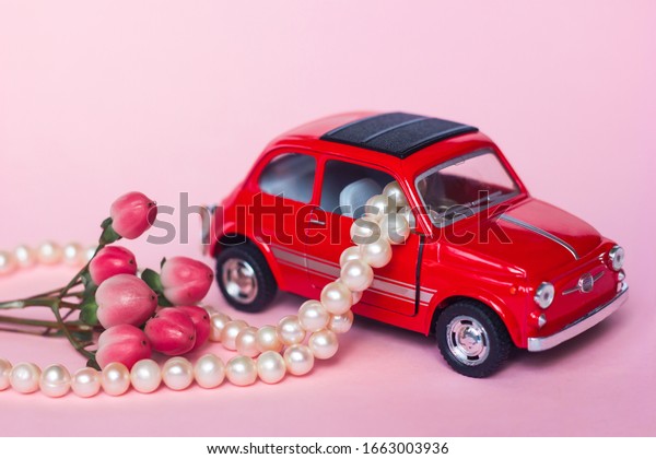 Red retro toy\
car delivers adefocused bouquet and a gift box on a blue\
background. Valentine\'s Day, February 14, greeting card.\
International Women\'s Day March 8,\
Mother\'s
