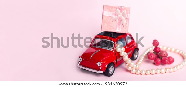 Red retro toy car delivers adefocused bouquet and a\
gift box on a blue background. Valentine\'s Day, February 14,\
greeting card. International Women\'s Day March 8, Mother\'s, copy\
space for text